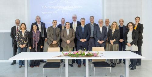 group photo of the participants of the 2026 EIROforum DG assembly. They stand in front of a screen. A table in front of them holds flowers.
